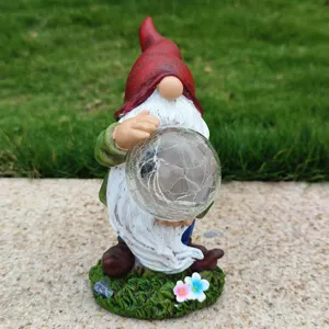 Resin garden gnome holding cracked glass solar ball, close-up outdoor decor detail.