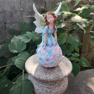 Resin angel fairy garden figurine sitting on a pastel rose ball, outdoor garden detail view.