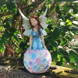 Detail view of garden angel fairy figurine sitting on pastel rose ball for outdoor decor.