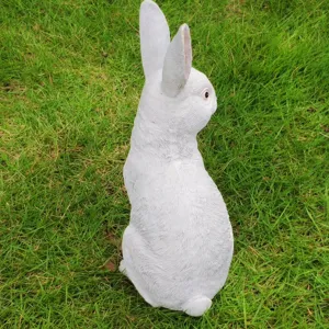 Detailed view of white rabbit garden statue, cute lawn ornament placed on green grass for yard decor.