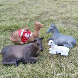 Detailed shot of resin animal figurines set including camel, ox, donkey, and sheep on grass.