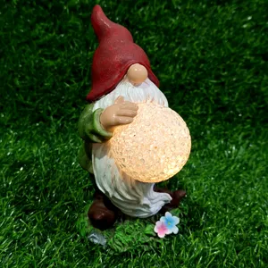 Solar garden gnome detail view showing the glowing cracked glass ball light on green grass texture.
