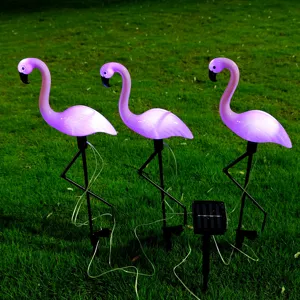 Detail view of solar-powered flamingo LED garden lights glowing brightly on a green lawn.