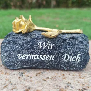 Memorial grave stone decoration with golden rose and engraved German text for cemetery remembrance.