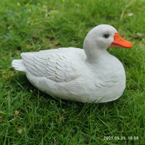 Detailed view of a cute white duck figurine sculpture placed on green grass for garden decor.