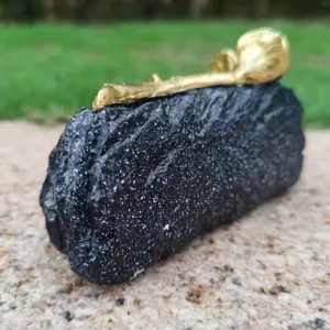 Detailed view of the black stone-textured memorial grave marker with a golden rose on top.
