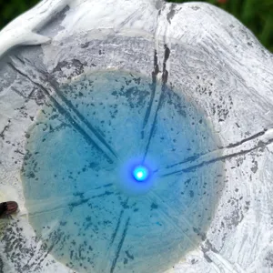 Close-up detail view of resin garden solar light showing blue glowing LED center and stone texture.