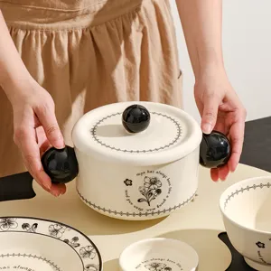 Detailopname van een keramisch servies met elegante bloemmotieven en zwarte bolvormige handgrepen.
