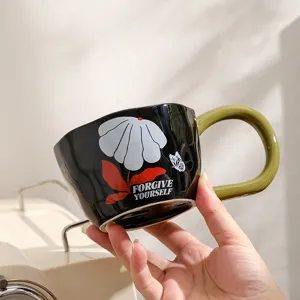 Ceramic coffee mug detail showing unique black body, green handle and floral typography.