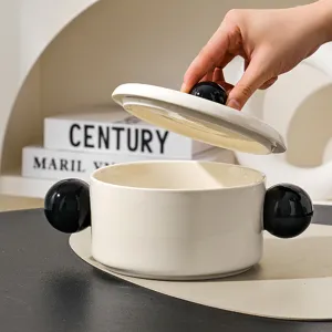 Modern ceramic double-ear soup bowl with lid and black sphere handles for kitchen use.