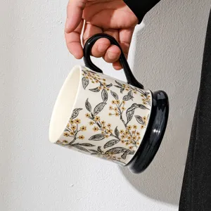 Handheld ceramic coffee mug with vintage botanical floral pattern and unique black handle and base.