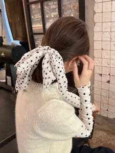 Primer plano detallado de un elegante coletero blanco con lunares y un lazo largo.