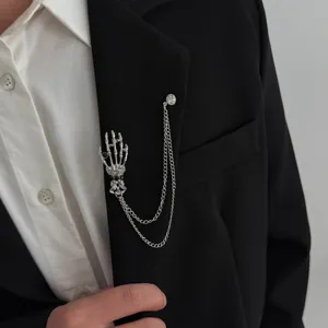 Close-up of rhinestone skeleton hand brooch with metal chains on black suit lapel detail.