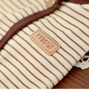 Close-up detail of striped pet clothing fabric with snap button and decorative leather logo patch.