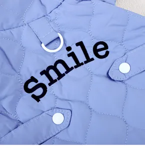 Close-up detail of light blue quilted pet vest with D-ring, snap buttons and smile embroidery.
