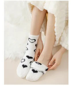 Close-up detail of cozy white fluffy fleece socks with black heart pattern for indoor use.
