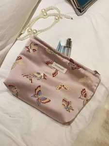 Close-up detail view of the pink satin cosmetic pouch featuring delicate embroidered butterflies.