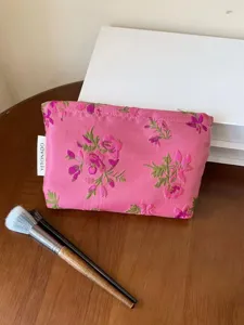Pink floral embroidered cosmetic bag detail, portable makeup pouch with zipper closure.