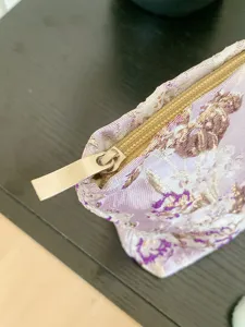 Detailed shot of purple floral embroidered cosmetic bag, showing fabric texture and zipper pull.