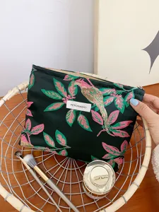 Detail shot of the dark green embroidered cosmetic bag with bird and leaf design patterns.