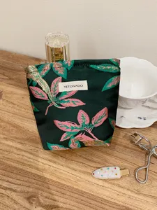 Detailed close-up view of the dark green leaf-patterned cosmetic pouch with brand tag.