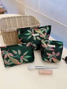 Detail view of dark green embroidered cosmetic bags set with elegant floral and bird patterns.