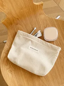 Detailed close-up of a beige corduroy cosmetic pouch placed on a wooden background with brushes.