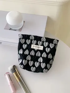 Detailed view of a black 3D silver heart cosmetic bag with branded tag and makeup brush props.