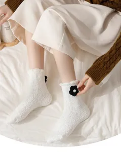 Nahaufnahme flauschiger weisser Korallenfleece-Socken mit schwarzer Blume, warm und bequem.