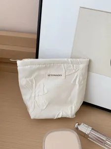 Vue détaillée de la trousse de maquillage blanche avec broderie nœud et étiquette tissée.