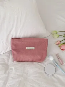 Pink corduroy cosmetic bag detailed close-up shot on white bedding with tulip and makeup props.