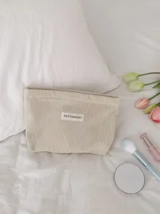 Detailed view of a beige corduroy makeup bag styled with tulips and cosmetics on a white bed.
