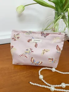 Pink butterfly brocade makeup bag detail showing elegant pattern and woven label on wooden table.