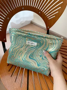 Detailed view of the luxury jacquard cosmetic pouch, showing intricate gold and teal texture.