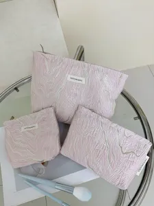 Close-up of pink textured cosmetic storage bags set, elegant jacquard pattern design detail.