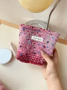 Close-up detail shot of the pink tweed cosmetic pouch showing textured fabric and zipper.