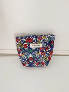 Close-up detail of a vintage floral cosmetic pouch with a white brand label and zipper.