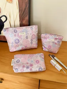 Detailed view of pink floral cosmetic bag set on wooden table with brushes for daily travel.