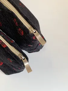 Close-up detail of black patterned cosmetic bag with silver metallic zipper and textured fabric.
