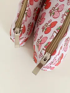 Close-up detail of the cute strawberry print fabric storage pouch featuring smooth metal zippers.