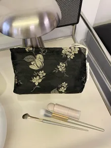 Detailaufnahme der eleganten schwarzen Kosmetiktasche mit Blumenmuster und Pinseln.