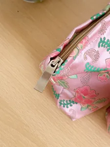 Close-up detail of the pink floral jacquard fabric and metal zipper on the cosmetic bag.