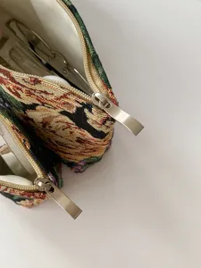 Detailed view of vintage floral embroidered cosmetic pouch with metal zipper on white background.