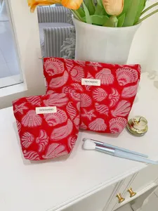 Detail view of the red shell pattern cosmetic makeup storage bag set on white table.