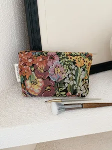 Detailed view of vintage embroidered jacquard cosmetic bag with makeup brushes in scene.