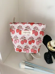 Close-up detail shot of the cute strawberry print cosmetic pouch with zipper and brand label.