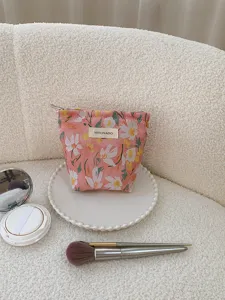 Detail shot of a pink floral embroidered cosmetic bag resting on a white tray with makeup brushes.