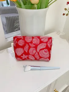 Red shell pattern makeup pouch detail view with cosmetic brush on white desk surface