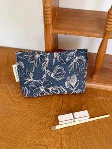 Detailed shot of a stylish blue floral cosmetic bag on a wooden surface with makeup tools.
