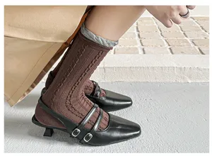 Women's brown cable-knit mid-calf socks with grey bubble cuffs paired with black Mary Jane shoes.